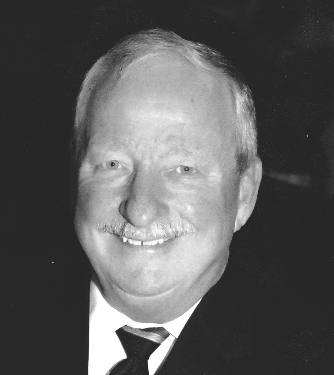 Black and white photo of a person with short, gray hair wearing a suit and tie.