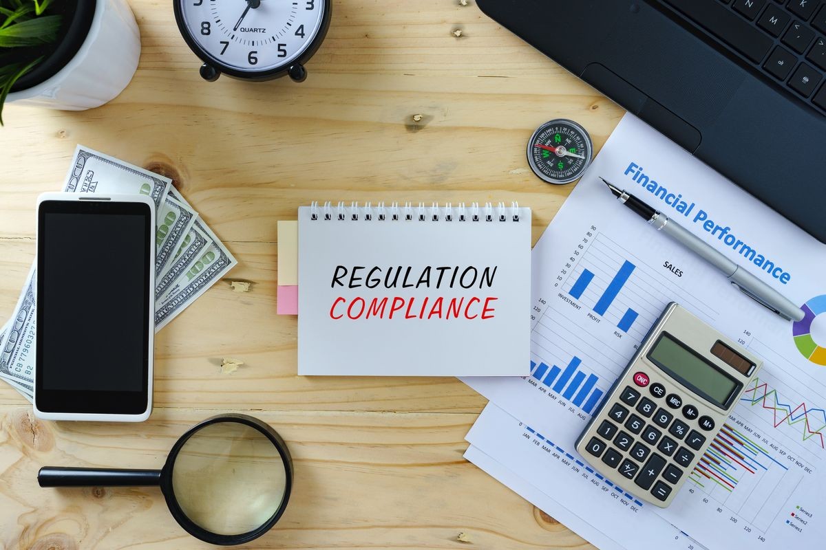 Business concept.Top view of working table with laptop, calculator, chart, smartphone, magnifying glass, clock, compass, pen and banknotes.Word REGULATION COMPLIANCE written on notepad.